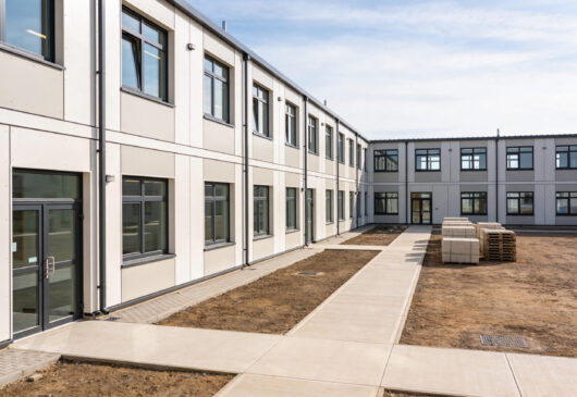 A contemporary modular building complex with clean lines, large windows, and an unfinished outdoor area awaiting landscaping